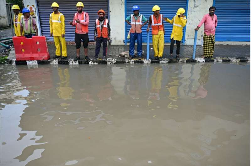 Men stand along a flooded street in Chennai on December 3