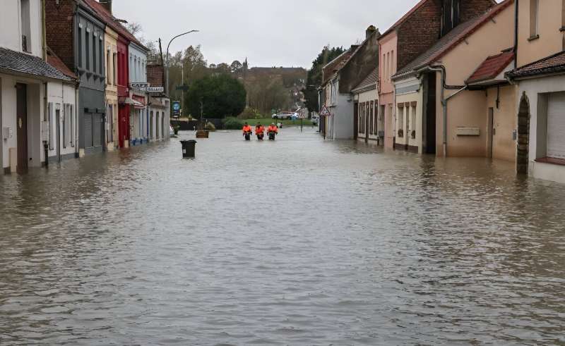 Municipal employees from Neuville-sous-Montreuil, northern France, walk down a flooded street