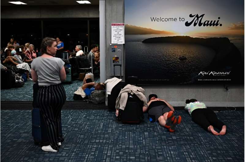 Passengers try to sleep below a 'Welcome To Maui' billboard on the floor of the airport terminal while waiting for evacuation fl