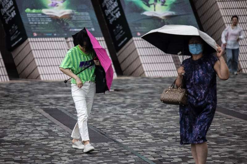 People holding tightly to umbrellas walk near Victoria Harbour as Typhoon Talim passes near Hong Kong on July 17, 2023