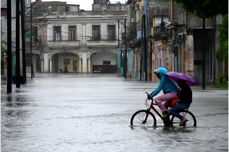 People ride a bicycle through a flooded street in Havana, on August 29, 2023, during the passage of storm Idalia