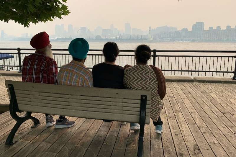 People sit on a bench taking in the smokey Montreal skyline