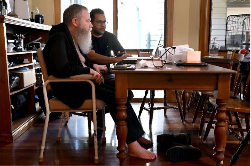 Rodney Gorham, que tem um implante cerebral Synchron, trabalha em um computador em sua casa em Melbourne com o engenheiro de campo clínico Zafa