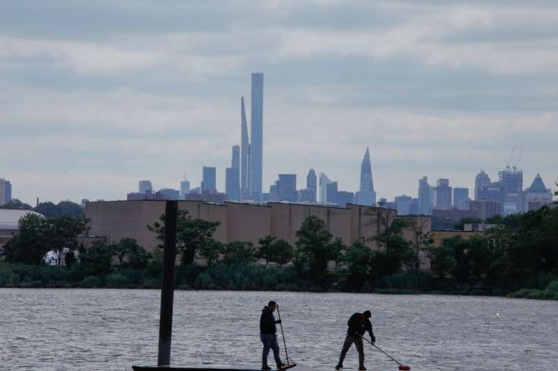 The New York City skyline looms behind workers cleaning a pier along the Hackensack River