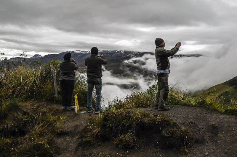 Tourists take photos of the Nevado del Ruiz volcano as it emits plumes of smoke