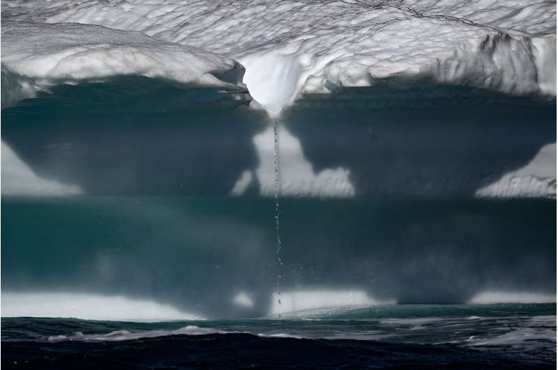 Water falling from a melting iceberg drifting along the Scoresby Sound Fjord, in Eastern Greenland