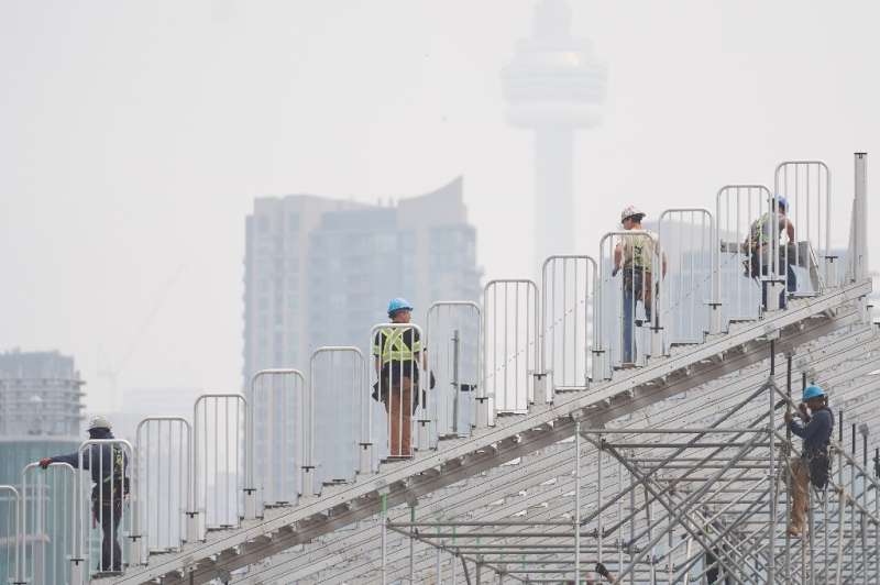 Workers assemble temporary grandstands for the Toronto Grand Prix as smoke rolls in