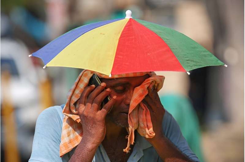 A vendor with an umbrella over his head talks on mobile phone as he wipes his face with a cloth on a hot summer day in Varanasi on May 27
