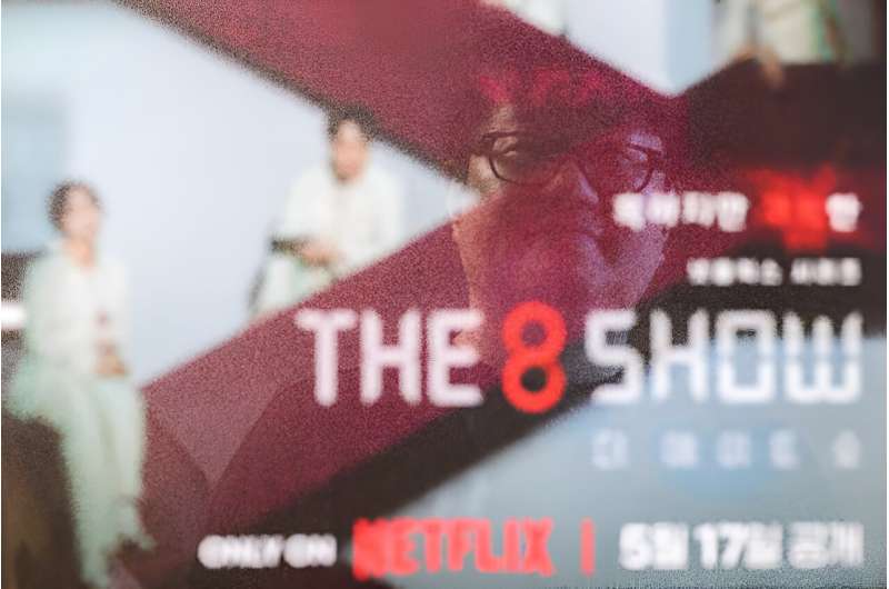 Bae Jin-soo, who created the Naver webtoons &quot;Money Game&quot; and &quot;Pie Game&quot; which inspired Netflix's &quot;The 8 Show&quot;, poses in front of a framed poster for the show