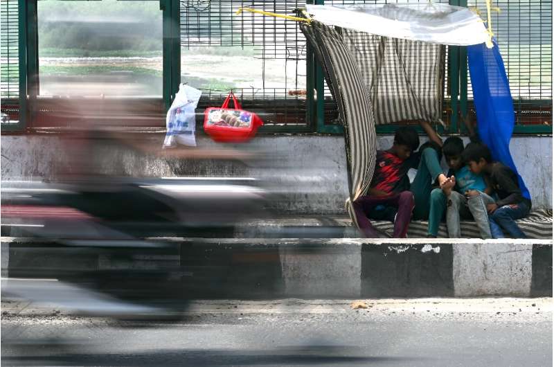 Boys sit beneath a makeshift canopy along a street on a hot summer day in New Delhi