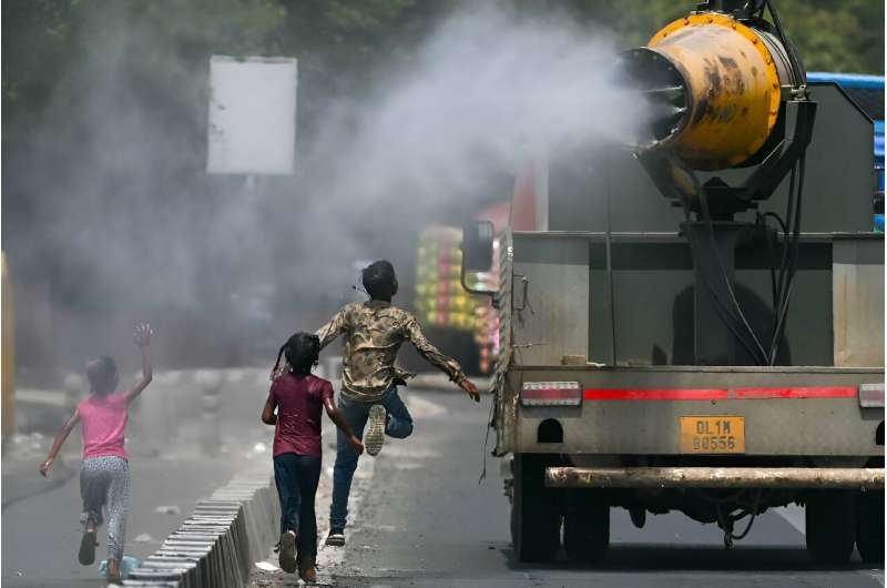 Children run behind a truck spraying water along a street on a hot summer day in New Delhi on Tuesday