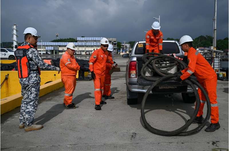 Coast guard personnel carry a suction hose for deployment at a port in Limay