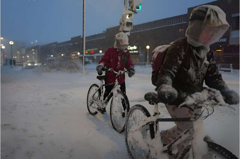 Cyclists navigate a snow-covered sidewalk on in Iowa City, Iowa