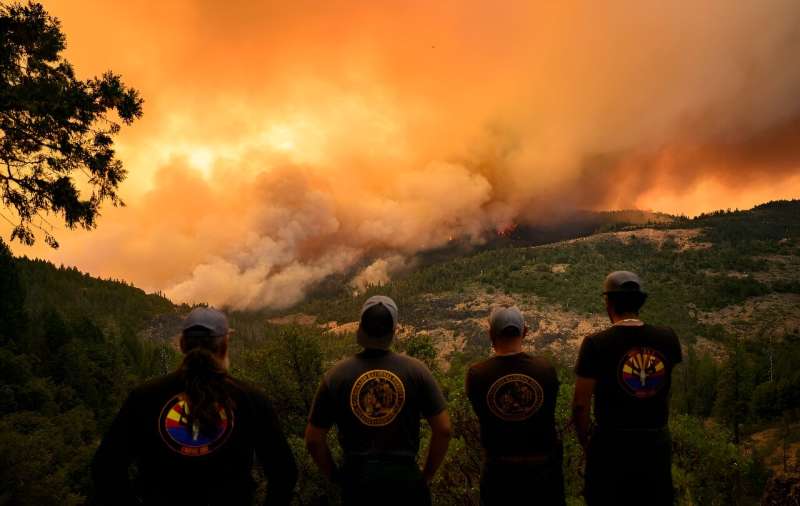 Firefighters watch as flames and smoke move through a valley in Butte County, California on July 26, 2024