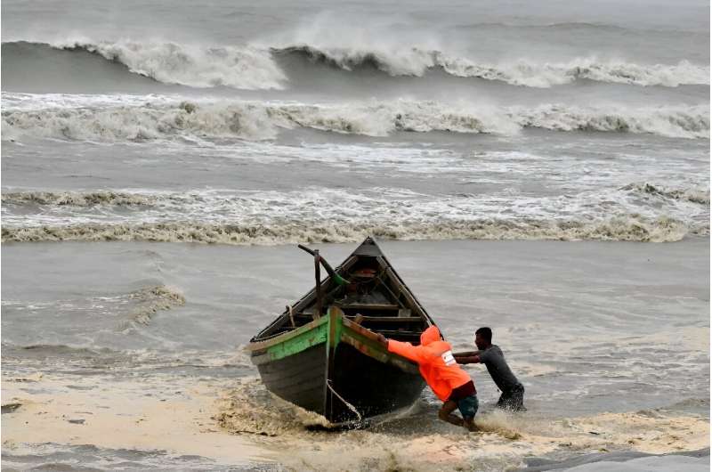 Men push a fishing boat to a sea shore as a preventive measure during rainfall in Kuakata on May 26, 2024, ahead of cyclone Remal's landfall in Bangladesh