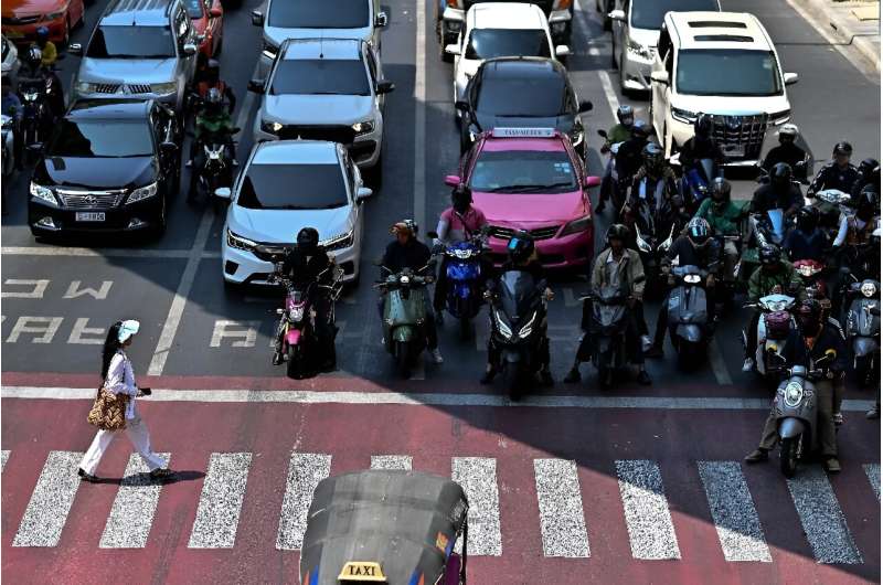 Motorcyclists wait under the shade at a traffic intersection in Bangkok