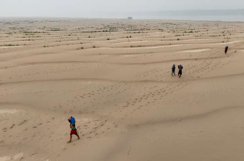 People carry drinking water along a sandbank of Madeira River in Paraizinho Community, in Humaita, Amazonas state, northern Brazil, on September 7, 2024