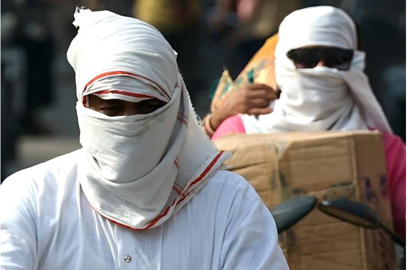 People riding bikes cover their faces with cloth on a hot summer afternoon in Varanasi on May 29