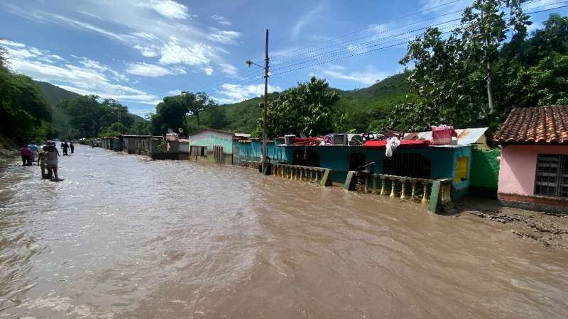 People stand outside their flooded homes after a river swelled due to heavy rains following the passage of Hurricane Beryl on the road from Cumana to Cumanacoa, Sucre State, Venezuela, on July 2, 2024