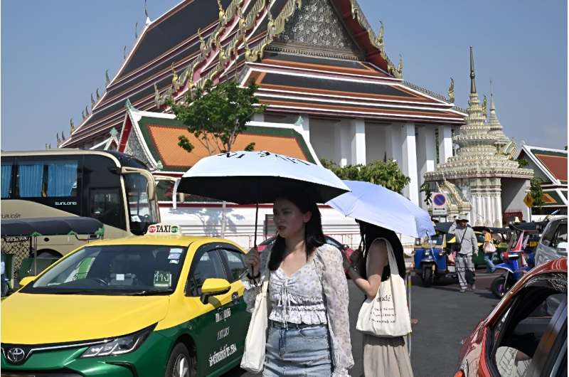 Tourists in this file photo shield themselves from the sun outside the Wat Pho Buddhist temple in Bangkok, where authorities have issued an extreme heat warning