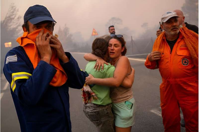 Frauen umarmen sich, nachdem sie am 11. August 2024 in Varnavas nördlich von Athen aus einem Waldbrand gerettet wurden