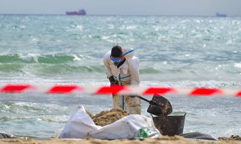 Workers in protective coats and masks shovelled sand tainted with an unidentified black substance into plastic sacks