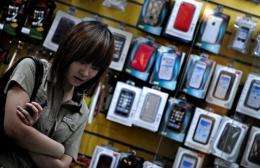 A woman stands in front of a shop selling mobile phone accessories in Shanghai