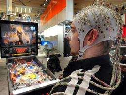 Crowds gathered round a man sitting at a pinball table, wearing a cap covered in electrodes attached to his head