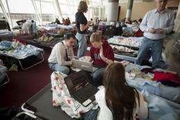 Stranded travelers use laptop computers while sitting on cots at JFK's Terminal 4