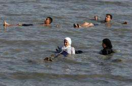 Two Palestinian Muslim women swim in their clothes in the waters of the Dead Sea